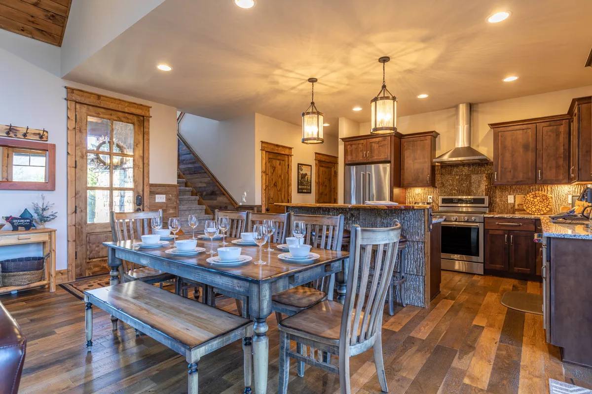 A close view of the kitchen and dining area, with a wooden dining table set for a meal, a spacious kitchen counter, high-end stainless steel appliances, and warm wooden cabinetry. The inviting setup highlights the kitchen's role as a gathering place for both meal prep and casual dining.