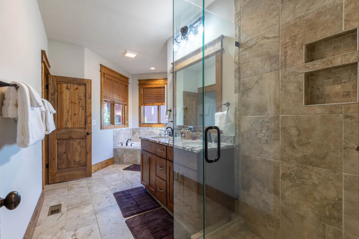 A bright bathroom featuring a glass-enclosed walk-in shower, double vanity with sleek sinks, and abundant natural light from windows. The space feels fresh, modern, and spa-like.