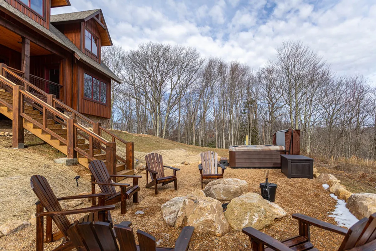 A private wooden deck with a luxurious Bullfrog Spas hot tub, surrounded by natural rock formations and adirondack chairs for fireside gatherings. The tranquil setting offers beautiful sunset views and the promise of starlit relaxation after an evening of games.