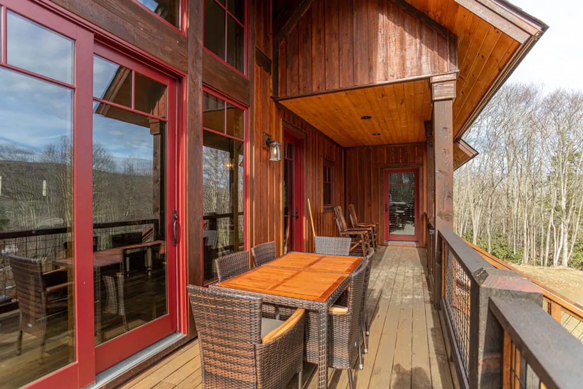 A welcoming wooden deck adorned with red-framed doors and comfortable outdoor furniture, surrounded by lush greenery. The image evokes a warm, communal atmosphere, ideal for casual dining, relaxing with a book, or group gatherings at sunset or under the stars.