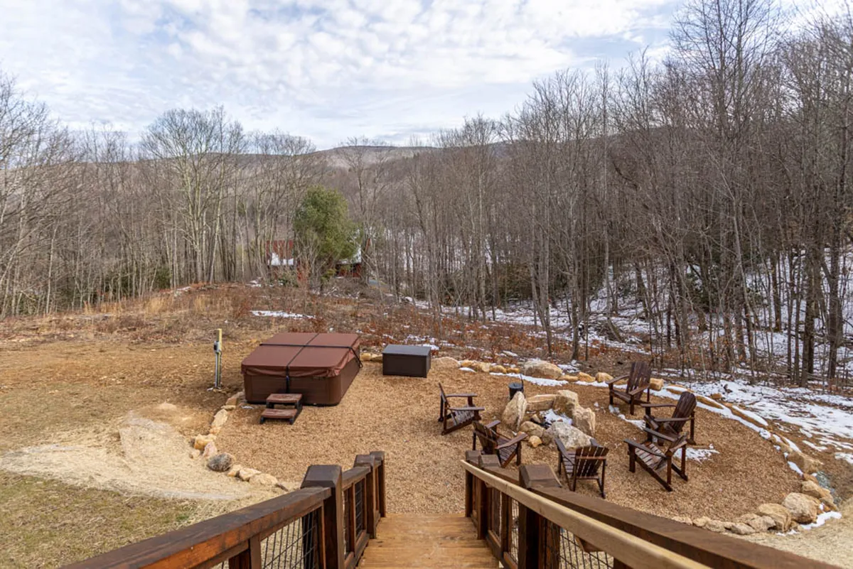 A serene exterior featuring a bubbling hot tub and adjacent seating area, enveloped by towering trees and mountain vistas. The space blends opportunity for relaxation with natural beauty, reflecting the peaceful moments available between the excitement of resort activities.
