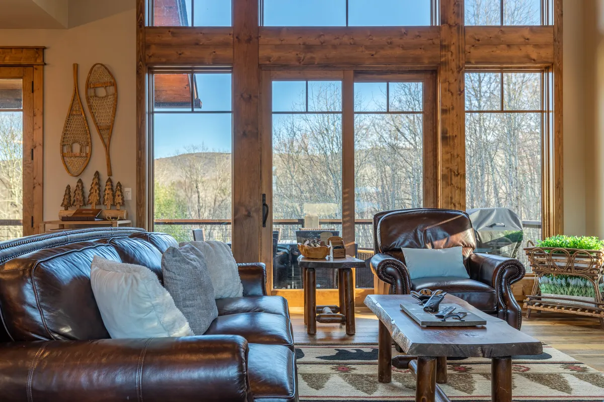 A sun-drenched living space with large windows letting in plenty of natural light, leather sofas, and a rustic wooden coffee table. The layout suggests a great spot for pet owners and their dogs to relax after a walk or outdoor play.