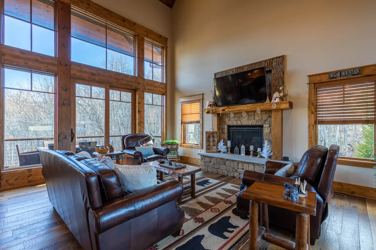 A cozy living area featuring large windows that frame views of the outdoors, a glowing fireplace, comfortable seating, and thoughtful decorative elements on the mantel. The space radiates warmth and relaxation, perfect for unwinding after a day of outdoor activities with pets.