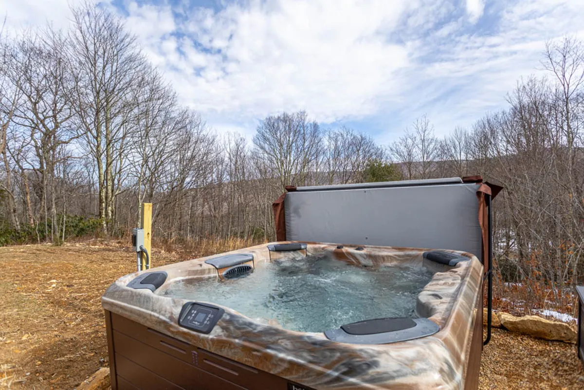 A tranquil outdoor hot tub set against a backdrop of surrounding nature and mountain views, inviting guests to relax, socialize, and stargaze. The mood is serene, emphasizing opportunities for late-night relaxation and connection.