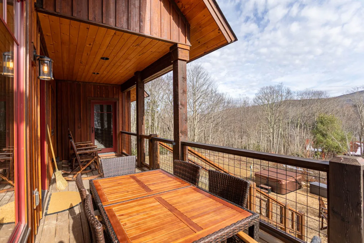 A large wooden deck featuring an outdoor dining table, surrounded by trees and with expansive mountain views. The scene suggests al fresco dining, morning coffee, evening gatherings, and nature observation, perfectly complementing social and communal experiences.