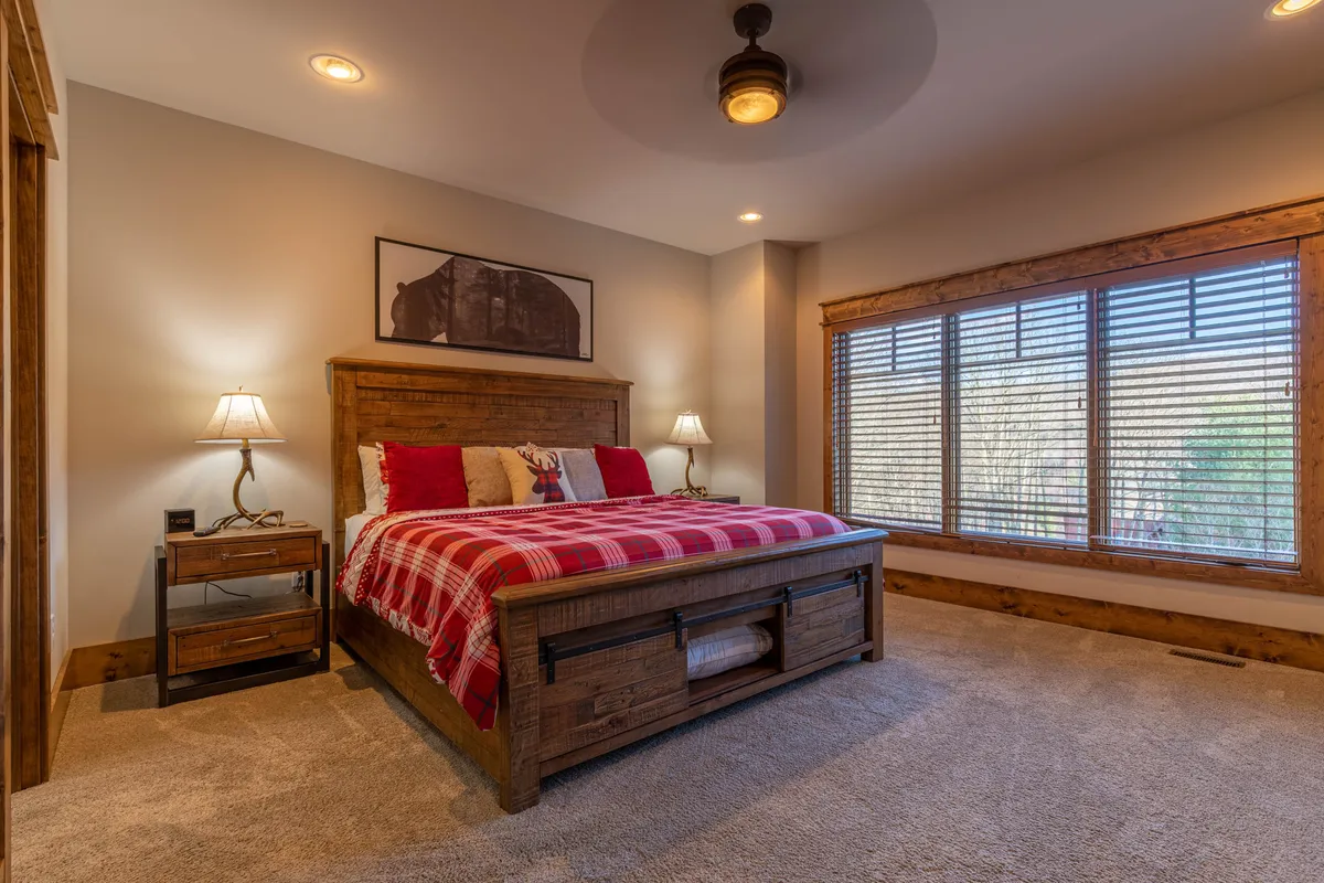 A warmly lit bedroom featuring a comfortable bed, matching nightstands, a large window providing natural light, and tasteful wall artwork. The cozy setup evokes a tranquil and inviting atmosphere ideal for rest.