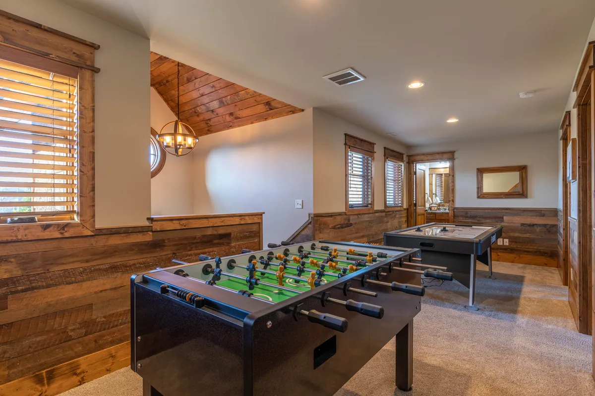 A recreation room with a foosball and pool table surrounded by wooden paneling and expansive windows that showcase the natural surroundings. The atmosphere is lively yet relaxed, inviting guests to enjoy fun evenings with friends or loved ones.