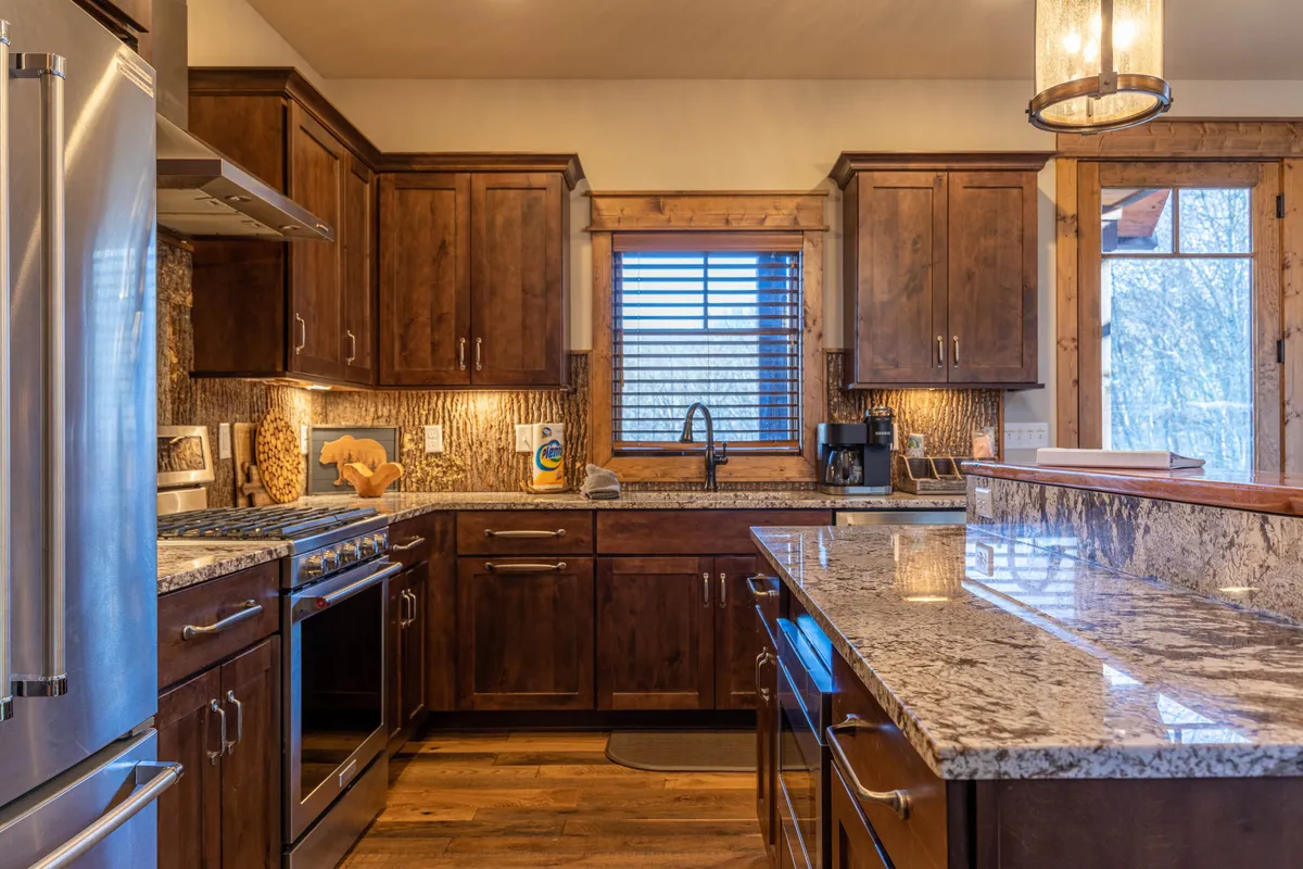 A warm, inviting kitchen with stainless steel appliances, granite countertops, and wood cabinetry. A window offers a view of the outdoors, suggesting a direct link between indoor comfort and outdoor adventure.